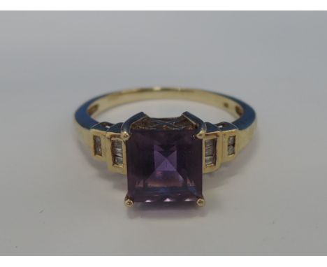 A ladies dress ring having a square cut purple stone in a raised stylised mount with small baguette and round cut diamonds to