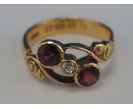 A ladies dress ring having two rubies intersppersed by a diamond in a stylised setting in a yellow metal engraved mount on a 