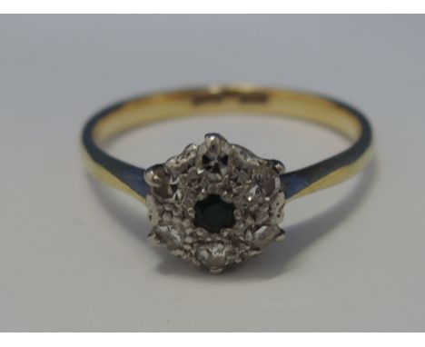 A ladies dress ring having a central emerald in a diamond daisy cluster on a yellow metal loop stamped 18ct Plat