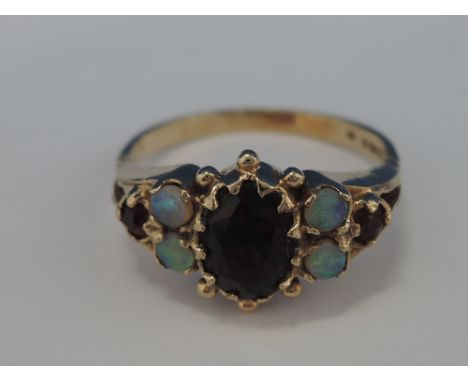 A ladies dress ring having a central oval garnet flanked by opals and further garnets in a moulded mount on a 9ct gold loop