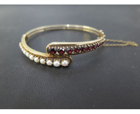 A 9ct gold half cultured pearl and garnet crossover style hinged bangle - Hallmarked London - Inner diameter 6.3cms - Weight 