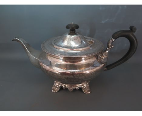 A George V silver teapot in the London style with ebony handle and lid finial decorative scroll work to quadripartite base wi