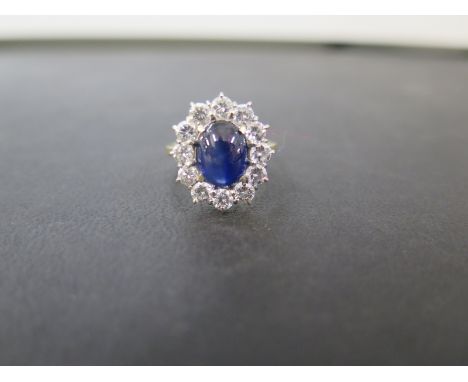 An 18ct gold sapphire and diamond cluster ring - The cabochon sapphire, displaying slight asterism within a brilliant-cut dia