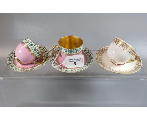 A pair of Royal Worcester pink ground and gilded cups and saucers with repeating floral and foliate border designs. Together 