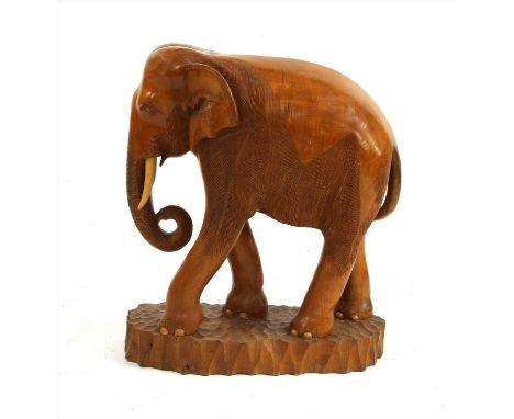 A carved teak elephant, 20th century, with a curled trunk and on an adzed base, 73cm high