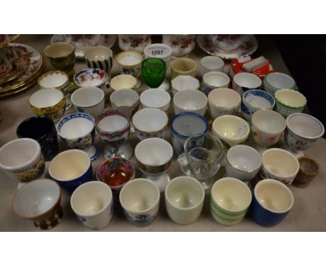 A quantity of ceramic and other egg cups to include Royal Crown Derby Posies, Cauldron Oriental, Willow pattern, novelty fire