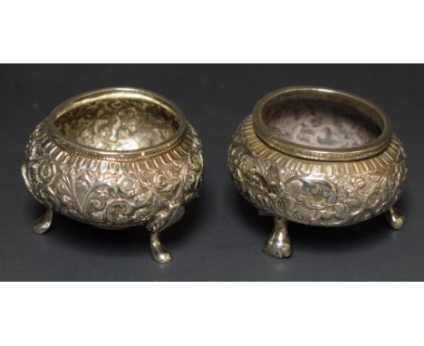 A pair Oriental/Burmese silver coloured metal open salts, all over repousse floral decoration, tripod feet (2) 