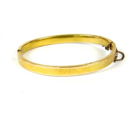 A hollow flat profile hinged bangle, (clasp broken), tested as approximately 9ct gold, with metal safety chain, 8,81g