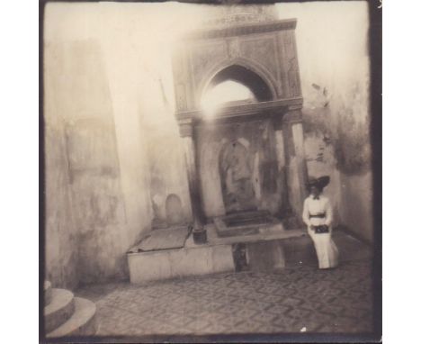 Silver gelatin black and white photograph with square format. Featuring a woman in a white button up dress and hat posing nex