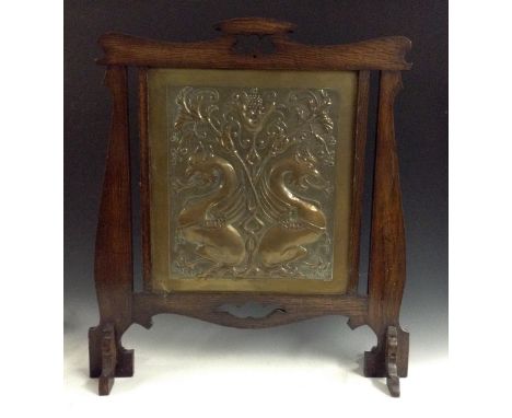 A Keswick School Arts and Crafts brass and treen firescreen, hammered in low relief with two fire breathing dragons surrounde