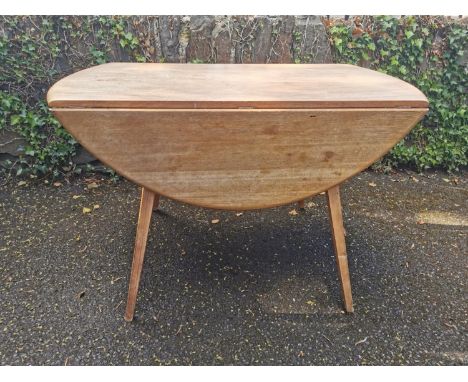 A light elm Ercol drop leaf table, of circular form on four legs, with paper label, 71 cm high x 113 cm wide x 113 cm diamete