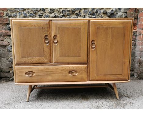 A small blonde elm Ercol sideboard, with twin cupboard doors above a single frieze drawer, flanked with a shelved cupboard, s