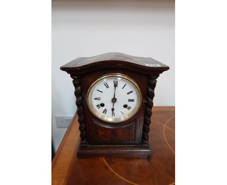 A 20th century oak cased mantle clock with white enamelled dial with Roman numerals to chapter ring flanked by applied barley