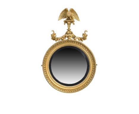 A Regency giltwood convex mirror, first quarter 19th century, the carved eagle crest perched upon scrolling foliage, the moul