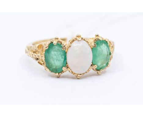 A 9ct gold opal and emerald ring, comprising a central oval opal set either side with oval cut emeralds, width approx 8mm, de