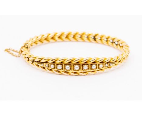 An early 20th century pearl and unmarked yellow metal bangle, rose twist design set to the centre with a row of graduated hal