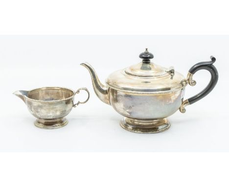 A George VI silver teapot and matching milk jug, plain bodies with beaded rim, the teapot with ebony handle and finial, hallm