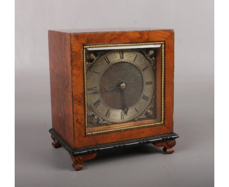 A burr walnut cased mantel clock. With brass square dial ornamented with spandrels and marked Made in England. With ebonized 