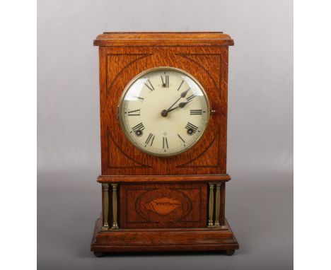 An American oak cased 8 day mantel clock. With brass column supports and marquetry shell patera. Having enamel dial signed Wm