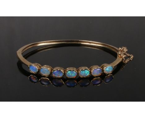 A 9ct gold bangle set with seven opals. Each stone housed within a lobed frame, 10.9 grams, 62mm wide.  