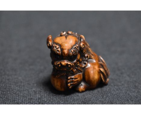 An early 20th century Japanese carved wood Netsuke of a Chinese mythical Pixiu with ball