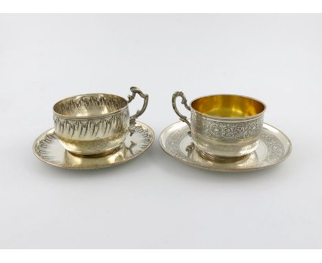 Two French silver cups and saucers, circa 1900, circular form, one with foliate scroll decoration, engraved with a monogram, 
