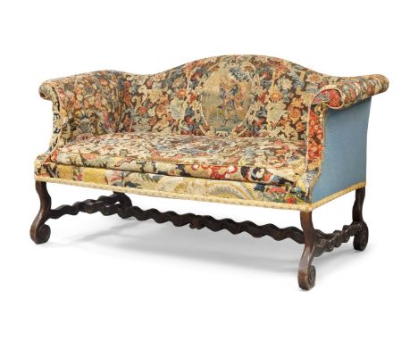 A Queen Anne oak framed camel back sofa, with tapestry upholstery, raised on scrolling supports, joined by wavy stretchers, 9