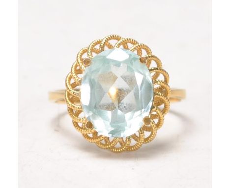 An 18k yellow gold ladies dress ring having a decorative scroll wire worked mount set with a central light blue oval cut ston