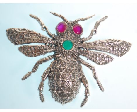 A stamped sterling silver bug brooch with moulded decoration set with ruby eyes and a round cut emerald. Measures 6cm wide. W