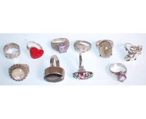 A group of ten silver rings to include a ring set with a faceted brown stone, a heart design ring set with red stones, a ring