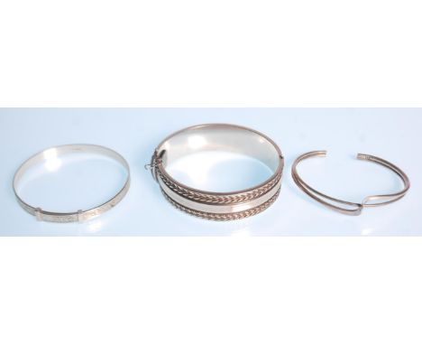 A group of three bangles to include a twist design bangle, a bangle with engraved foliate decoration and a wide bangle with f