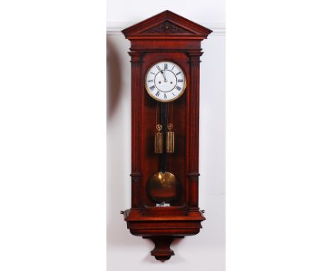 A late 19th century polished oak cased Vienna droptrunk wall clock, having an architectural pediment, white enamel dial with 