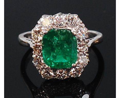 A platinum, emerald and diamond cluster ring, the four claw set octagon cut emerald weighing approx 2ct in a surround of twel