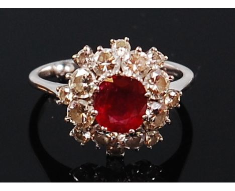 An 18ct white gold, ruby and diamond cluster ring, arranged as a raised centre claw set oval cut ruby weighing approx 0.85ct,