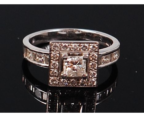 An Art Deco style 18ct white gold diamond ring, the centre four claw set princess cut diamond in a surround of pavé set small