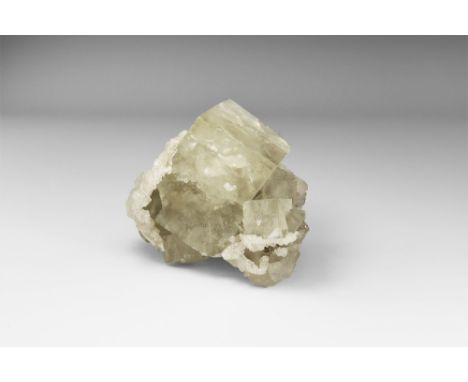 A fine cubic crystal of colourless fluorite resting on a number of smaller fluorite cubes, one side encrusted with white calc