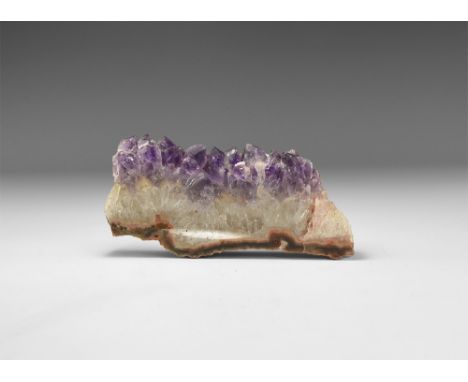 A large cut and polished slice of amethyst crystals on a matrix and with white crystals to the base; one side with a cut and 