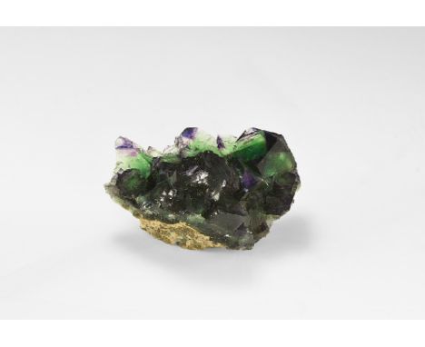 A large fluorite composed of several square crystals with stepped faces and purple-green colouring; in white card tray with G
