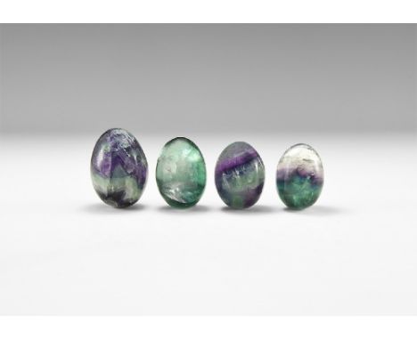 A group of four polished fluorite eggs showing bands of colour from clear to green and purple, and with rainbow reflections; 