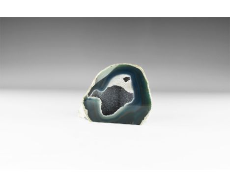 A large display geode, cut and polished to the side and base showing bands of blue, green and brown lined with clusters of sm