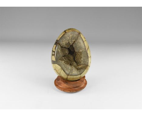 A large polished septarian egg with section cut to reveal internal cavity filled with clusters of small black crystals; mount