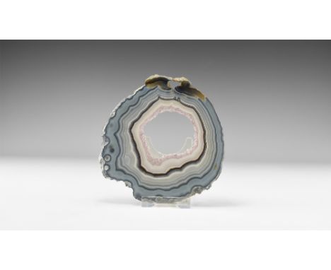 A cut and polished agate geode slice with variegated bands of blue, brown and black; centre open and the edges framed by clus