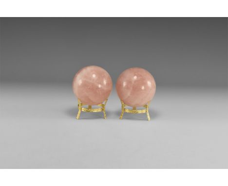 A pair of rose quartz spheres with deep pink colour and with white crystal bands; both with gilt metal tripod stands. See Bon
