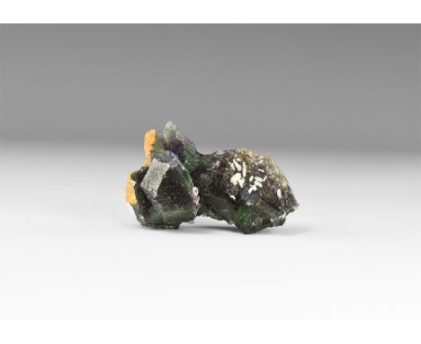 A dark green fluorite crystal with well formed faceted faces and calcite growths to one area, in white card tray with Gregory