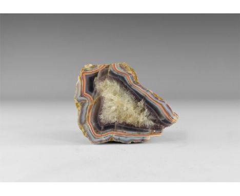 A cut and polished chunk of agate showing bands of blue, red and brown to the border, honeycomb quartz crystal growth to the 