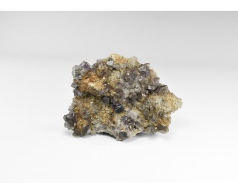 An English matrix specimen of purple fluorite cubes resting on a bed of small yellow and purple fluorite cubes, in old white 