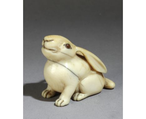 A mid 18th century Japanese netsuke from Edo period in carved elephant ivory portraying a hare with amber eyes looking upward