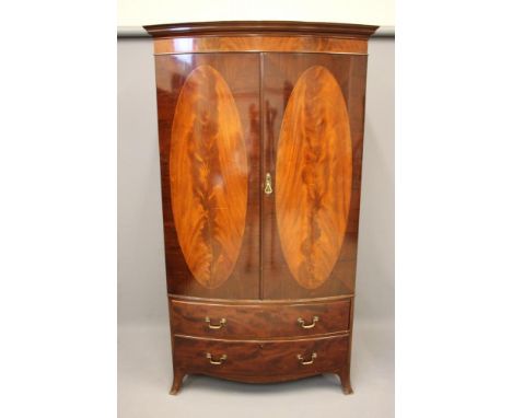 AN EDWARDIAN MAHOGANY BOW FRONT WARDROBE of Georgian design, moulded cornice over two doors each inlaid with an oval flame ma