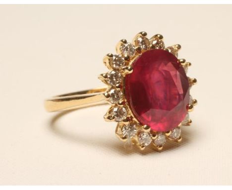 A RUBY AND DIAMOND CLUSTER RING, the oval cut ruby claw set to a border of sixteen small round brilliant cut diamonds, to a p