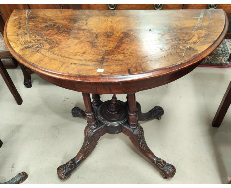 A Victorian figured walnut card table the demi-lune fold over top with marquetry inlaid decoration, on turned legs and carved